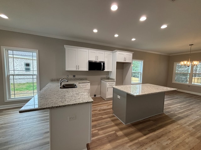 kitchen featuring sink, white cabinetry, hanging light fixtures, kitchen peninsula, and light stone countertops