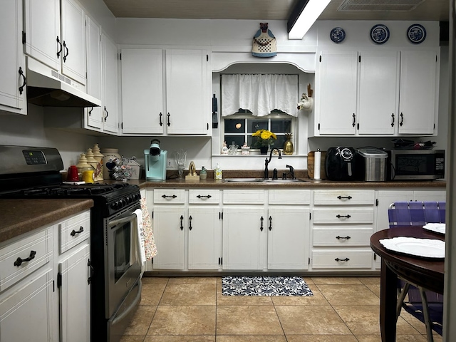 kitchen featuring dark countertops, appliances with stainless steel finishes, white cabinetry, a sink, and under cabinet range hood