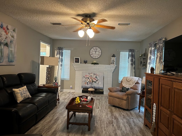 living area with a brick fireplace, a textured ceiling, visible vents, and wood finished floors