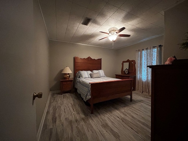 bedroom with ornamental molding, wood finished floors, visible vents, and a ceiling fan