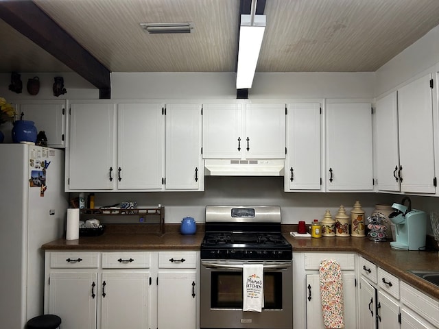 kitchen with dark countertops, freestanding refrigerator, white cabinets, under cabinet range hood, and stainless steel gas range oven