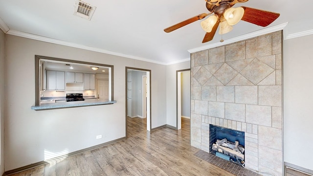 unfurnished living room featuring ceiling fan, ornamental molding, a tiled fireplace, and light hardwood / wood-style floors