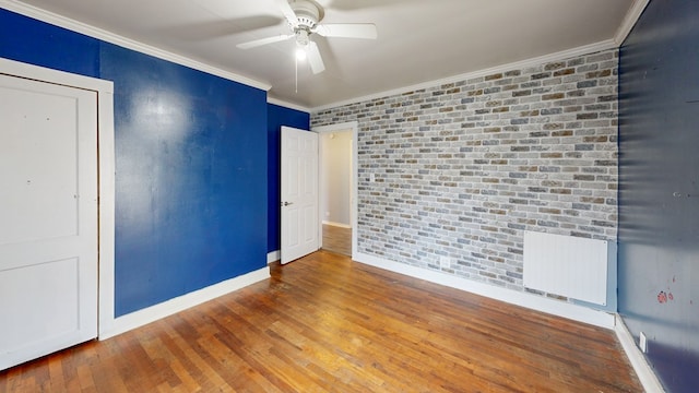 unfurnished room with radiator, wood-type flooring, ornamental molding, and brick wall