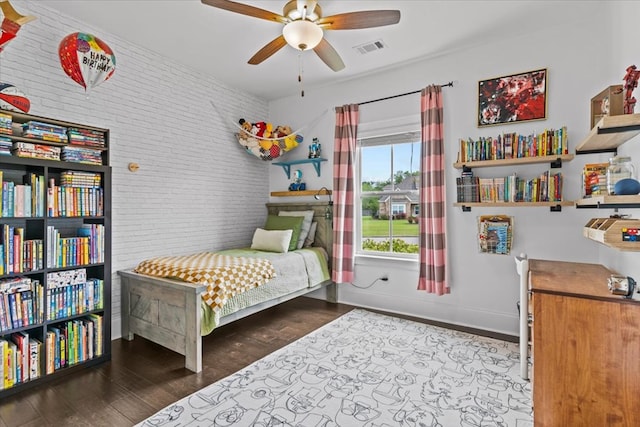 bedroom featuring visible vents, baseboards, wood finished floors, and brick wall