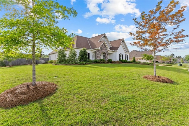 view of side of home with fence, a yard, and stone siding