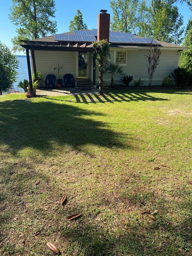 back of house with a patio, entry steps, a lawn, roof mounted solar panels, and metal roof