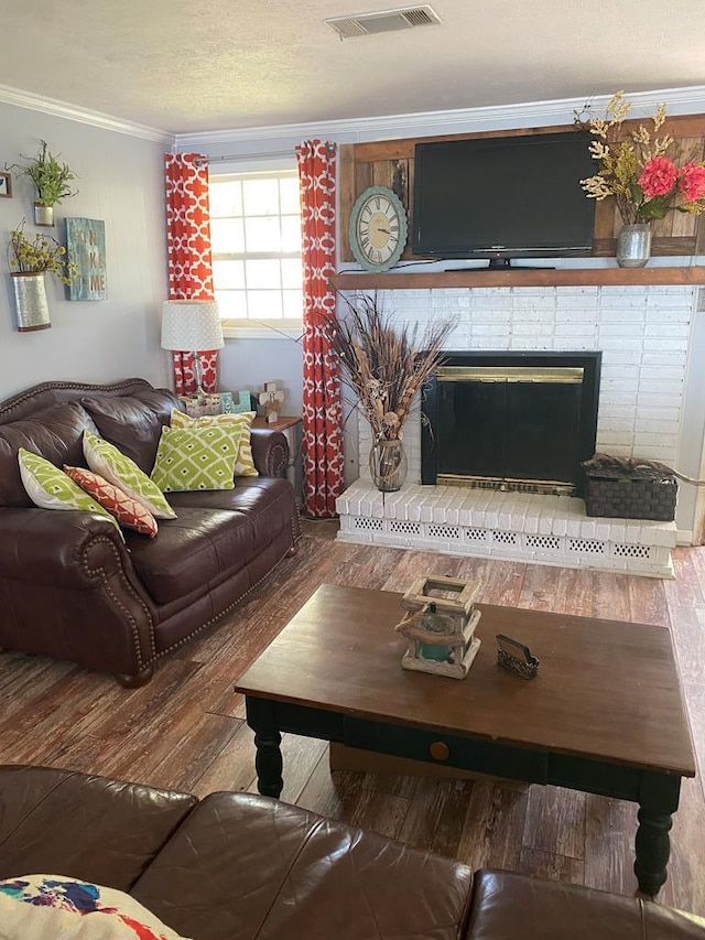 living area featuring visible vents, a textured ceiling, wood finished floors, crown molding, and a brick fireplace
