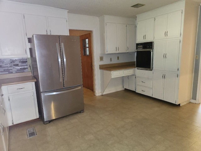 kitchen featuring decorative backsplash, a textured ceiling, white cabinetry, black oven, and stainless steel refrigerator