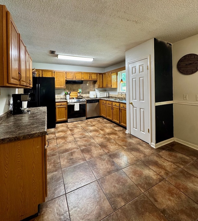 109 Pinehurst Dr, Ashford, AL 36312 - kitchen featuring appliances with stainless steel finishes, brown cabinets, dark tile patterned floors, a textured ceiling, and under cabinet range hood