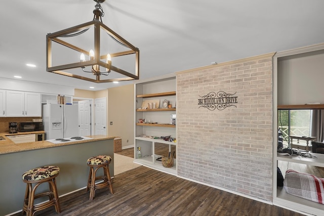 kitchen with brick wall, white cabinetry, kitchen peninsula, dark wood-type flooring, and white appliances