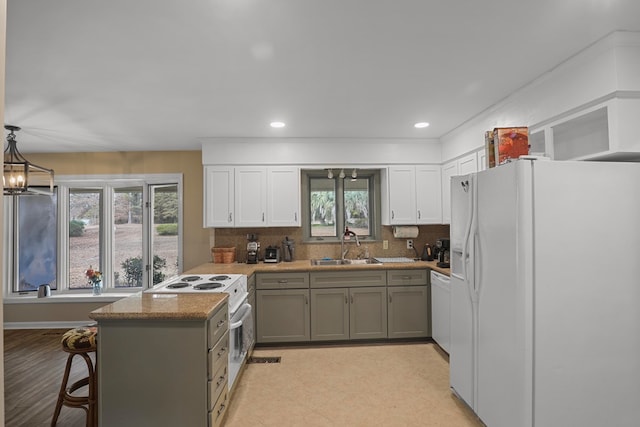 kitchen with sink, hanging light fixtures, kitchen peninsula, gray cabinets, and white appliances