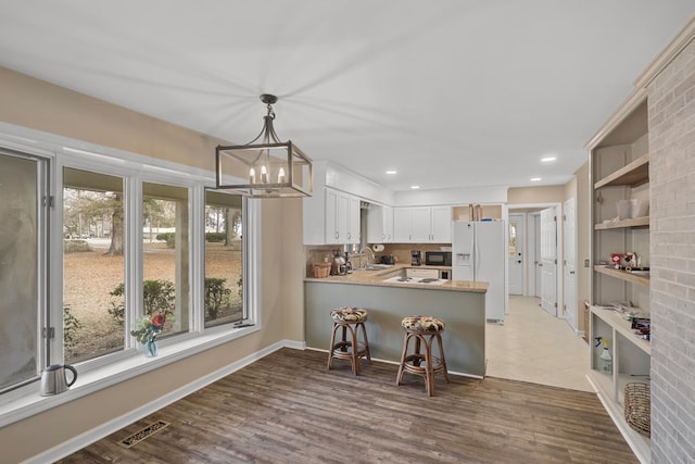 kitchen with white cabinetry, wood-type flooring, sink, white fridge with ice dispenser, and kitchen peninsula