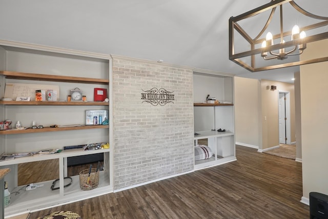 unfurnished living room featuring an inviting chandelier, dark wood-type flooring, and brick wall