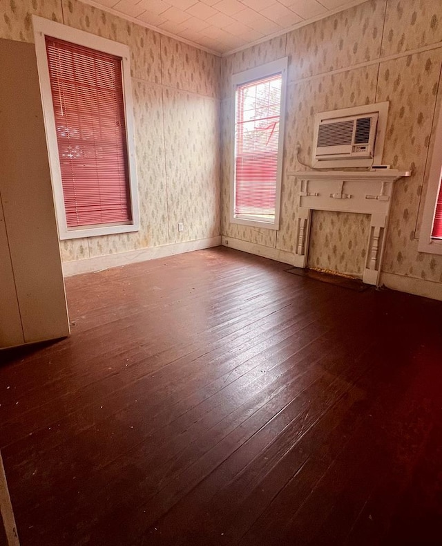 unfurnished living room with a wall unit AC, wood-type flooring, ornamental molding, baseboards, and wallpapered walls