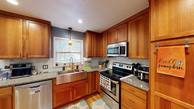 kitchen with sink, light wood-type flooring, light stone countertops, appliances with stainless steel finishes, and tasteful backsplash