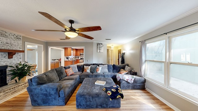 living room with a brick fireplace, light hardwood / wood-style flooring, ceiling fan, and ornamental molding