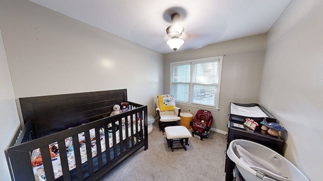 carpeted bedroom featuring ceiling fan and a nursery area