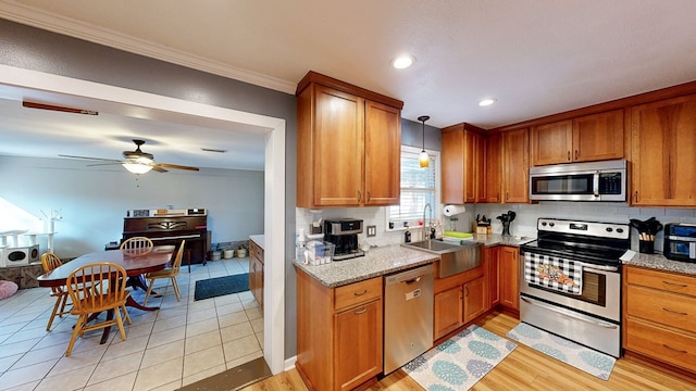 kitchen with light stone countertops, sink, stainless steel appliances, decorative light fixtures, and light tile patterned flooring