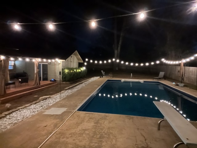 pool at night featuring a diving board and a patio area