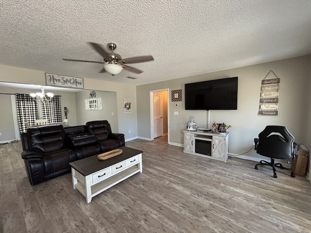 living area with wood finished floors, a textured ceiling, ceiling fan with notable chandelier, baseboards, and visible vents