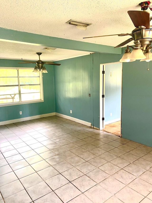 tiled spare room featuring wooden walls, a textured ceiling, ceiling fan, and visible vents