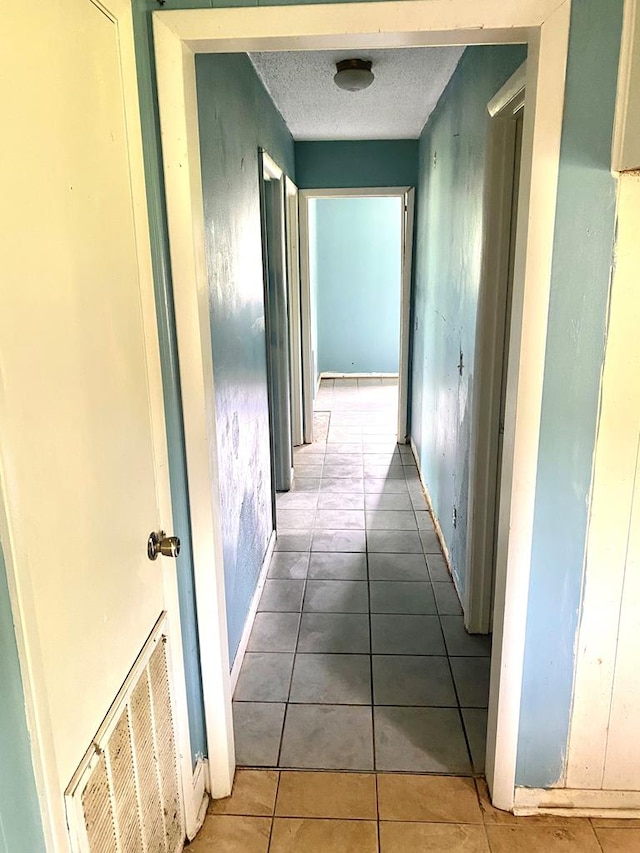 corridor with tile patterned floors, a textured ceiling, visible vents, and baseboards