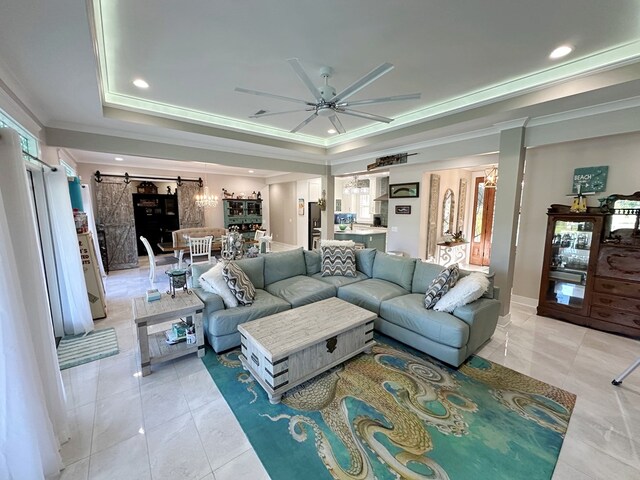 living room featuring a barn door, a tray ceiling, ceiling fan, and ornamental molding