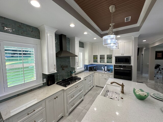 kitchen featuring backsplash, wall chimney range hood, appliances with stainless steel finishes, decorative light fixtures, and white cabinetry