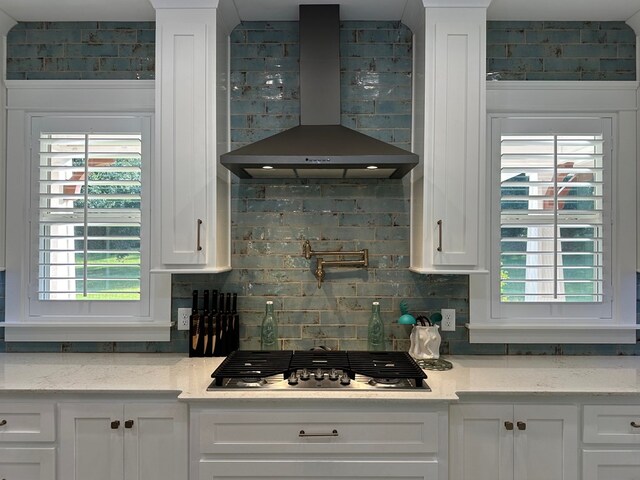 kitchen featuring light stone countertops, white cabinets, wall chimney range hood, and stainless steel gas cooktop