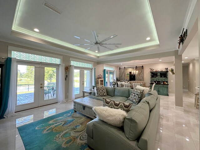 tiled living room featuring ceiling fan, crown molding, a tray ceiling, and french doors