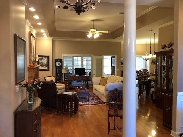 living room featuring a raised ceiling, ornate columns, dark wood-type flooring, and ornamental molding