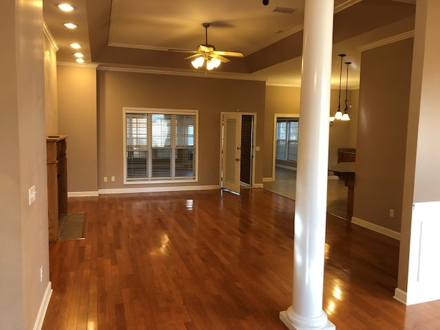 unfurnished living room featuring dark hardwood / wood-style flooring, decorative columns, a tray ceiling, and a healthy amount of sunlight