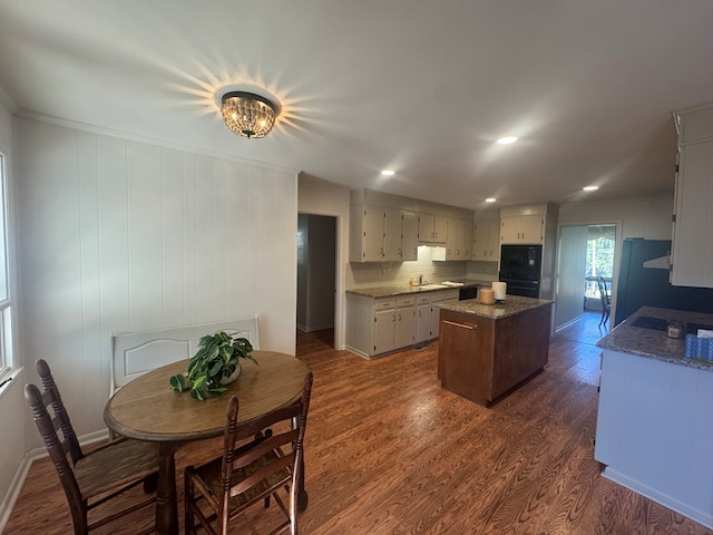 kitchen featuring a center island, black appliances, tasteful backsplash, stone countertops, and dark hardwood / wood-style flooring