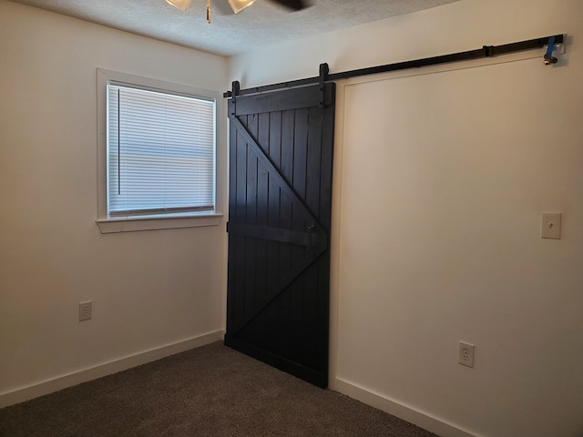 unfurnished room with dark colored carpet, a textured ceiling, a barn door, and ceiling fan