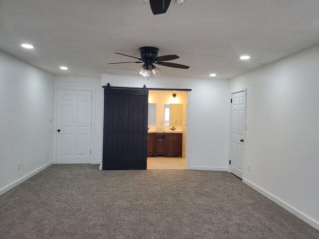 unfurnished bedroom featuring sink, ensuite bath, ceiling fan, a barn door, and carpet floors