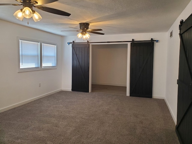 unfurnished bedroom featuring carpet, ceiling fan, a barn door, and a textured ceiling