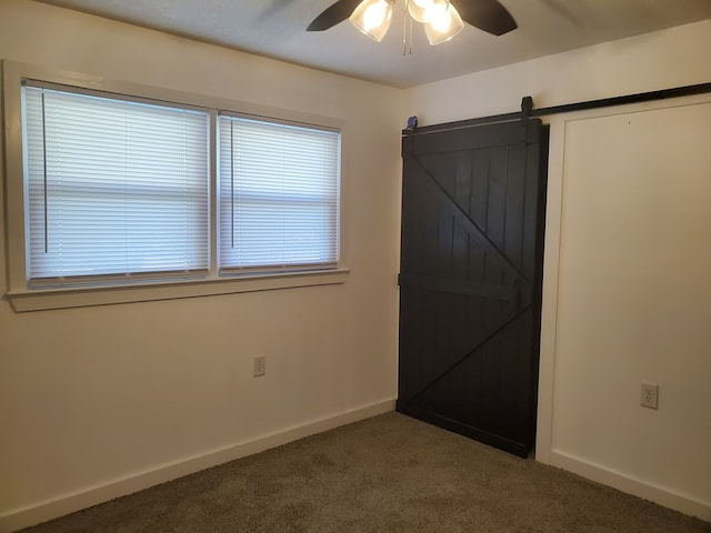 unfurnished room with carpet, a barn door, and ceiling fan