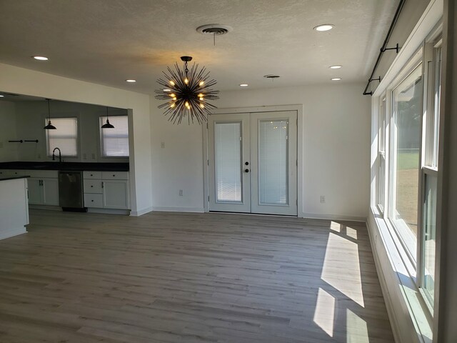 unfurnished living room featuring sink, french doors, an inviting chandelier, light hardwood / wood-style floors, and a textured ceiling