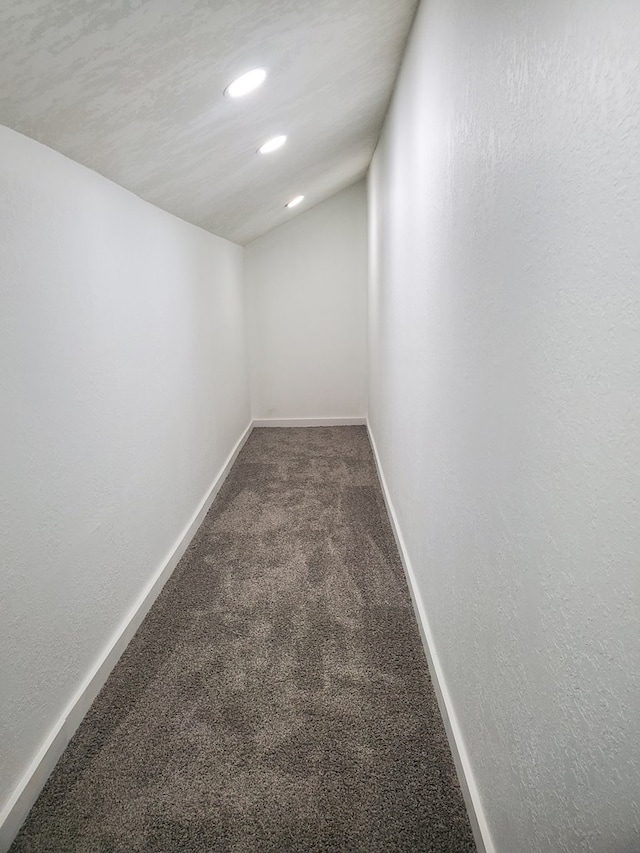 interior space with a textured ceiling, dark carpet, and lofted ceiling