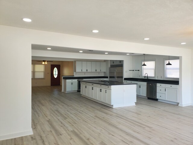 kitchen featuring appliances with stainless steel finishes, light wood-type flooring, a kitchen island with sink, ceiling fan, and decorative light fixtures