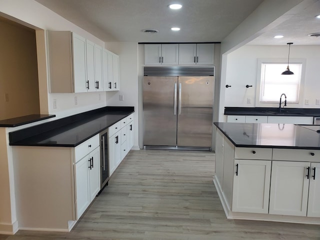 kitchen featuring sink, white cabinets, light hardwood / wood-style floors, hanging light fixtures, and built in fridge