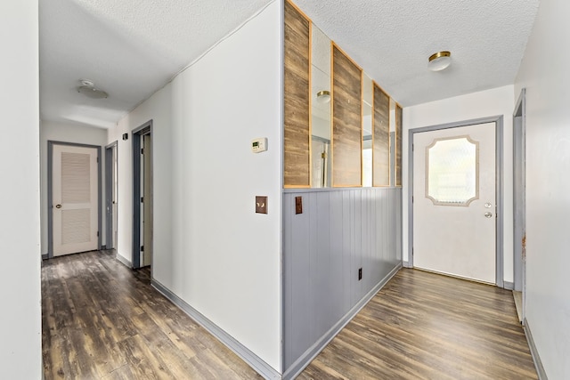 corridor with wooden walls, dark hardwood / wood-style floors, and a textured ceiling