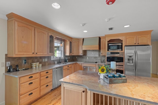 kitchen with light stone countertops, light brown cabinets, light hardwood / wood-style flooring, appliances with stainless steel finishes, and custom exhaust hood