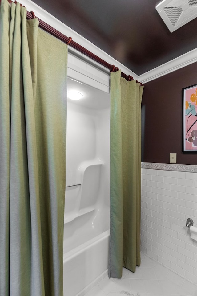 bathroom with tile patterned floors, tile walls, crown molding, and shower / tub combo