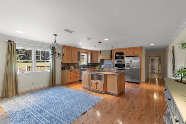 kitchen with custom exhaust hood, a kitchen island, ornamental molding, appliances with stainless steel finishes, and light hardwood / wood-style floors