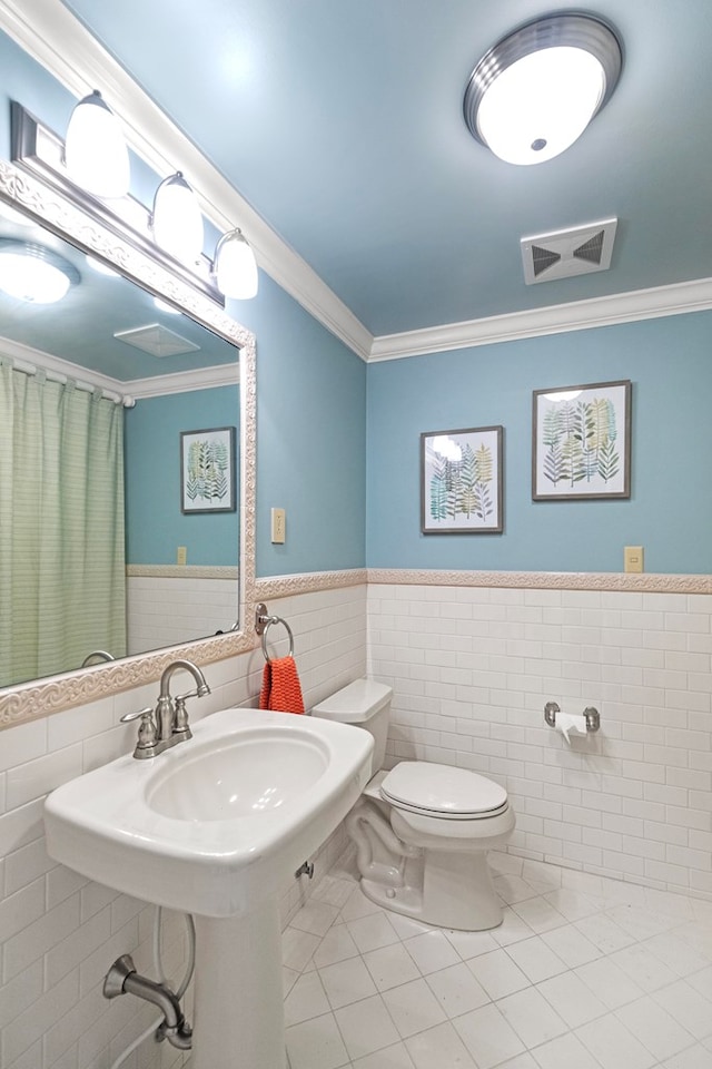 bathroom with tile patterned flooring, toilet, ornamental molding, and tile walls