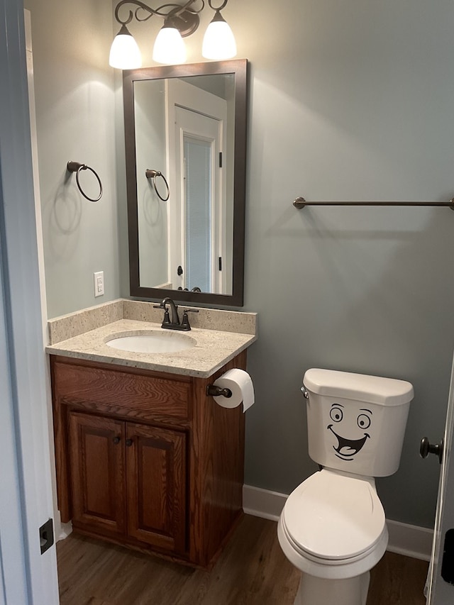 half bath with toilet, wood finished floors, and vanity