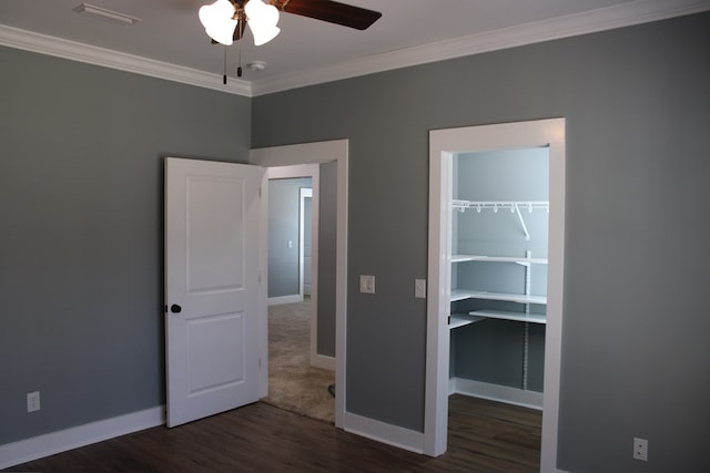 unfurnished bedroom with wood finished floors, baseboards, a closet, a walk in closet, and crown molding