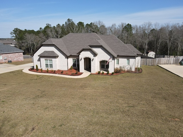 french provincial home with brick siding, fence, a front yard, and a shingled roof