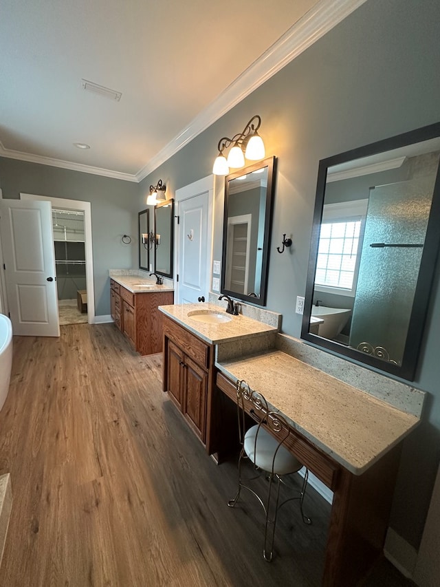 full bathroom with a sink, a freestanding tub, wood finished floors, and ornamental molding